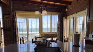 A kitchen with a large island, two pendant lights, and a view of the sea through large windows.