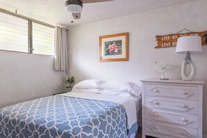 Un dormitorio con cama, cómoda, cuadro enmarcado, ventana con cortinas y un letrero en la pared.