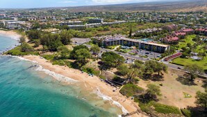 Vista aérea de una zona costera con una playa, un estacionamiento y un edificio de techo plano.