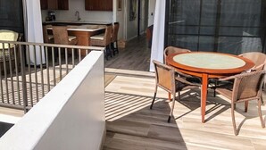 A balcony with wicker furniture, a kitchen in the background, and a sliding glass door.