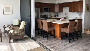 A modern kitchen with dark wooden cabinets, a central island with bar stools, a refrigerator, microwave, and a sink.
