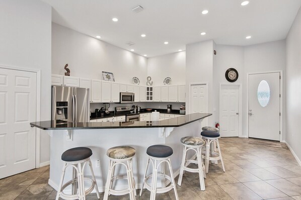 A modern kitchen with white cabinetry, a central island with bar stools, stainless appliances, and a decorative wall clock.