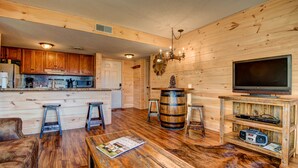 Een gezellig interieur in chaletstijl met houten wanden, een houten vloer, een barkruk, een salontafel, een televisie en een keuken met houten kasten en apparatuur.