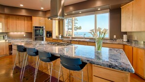 Una cocina moderna con una isla grande, taburetes de bar y vista al mar.