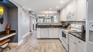 A modern kitchen with white cabinetry, a granite countertop, and a built-in oven. - Condo with Breathtaking Views on Water Park & 4 Free Passes, 4min Walk to Beach (Indian Rocks Beach)