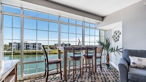A spacious balcony with a view of a river and buildings, furnished with a table and chairs, and a patterned rug on the floor. - Condo with Breathtaking Views on Water Park & 4 Free Passes, 4min Walk to Beach (Indian Rocks Beach)