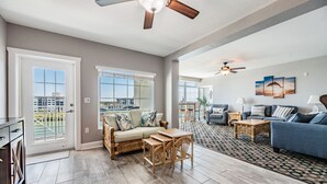 A spacious living area with a dining set, a blue sofa, and a ceiling fan. - Condo with Breathtaking Views on Water Park & 4 Free Passes, 4min Walk to Beach (Indian Rocks Beach)