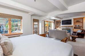 A spacious bedroom with a large bed, a fireplace, a TV, and a view of the outdoors.