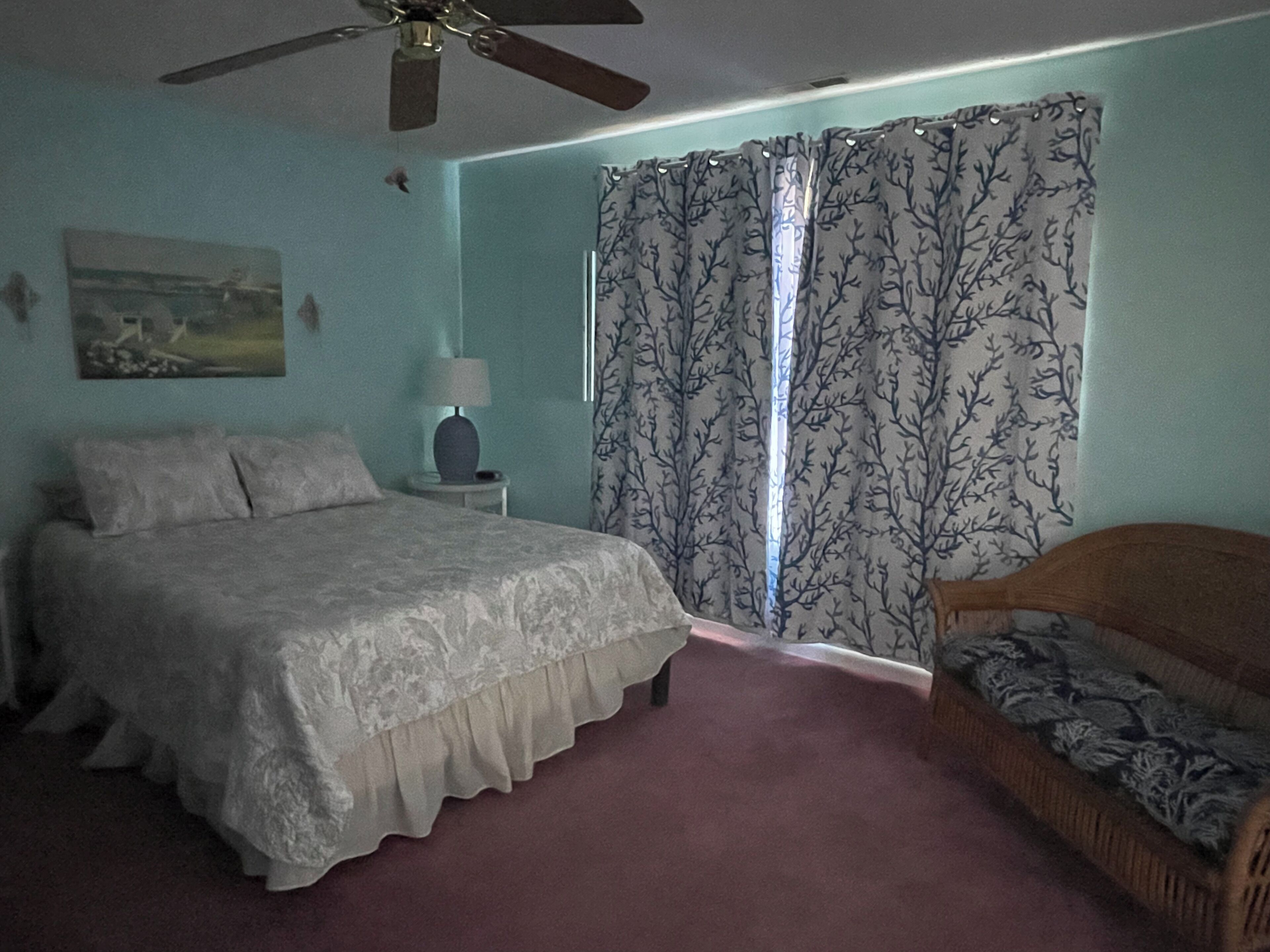 A bedroom with a bed, a nightstand, a lamp, a ceiling fan, and a window with curtains.