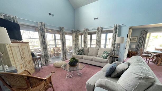 A spacious living room with a large window, a sofa, a coffee table, and a wicker chair. - 3 bedroom Family Friendly condo (Lewes)