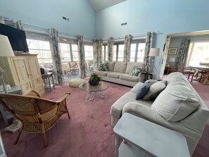 Ein geräumiges Wohnzimmer mit großem Fenster, einer Couch, einem Couchtisch und einem Korbsessel.