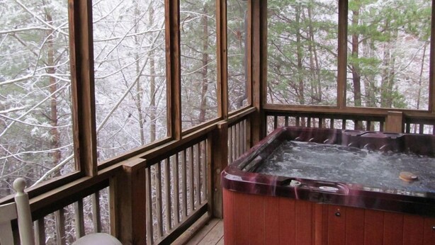 A hot tub on a wooden deck with large windows overlooking a snowy forest. - The Smoky Mountains are OPEN FOR BUSINESS. Recently remodeled on inside.  (Sevierville)