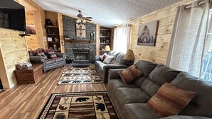 A cozy log cabin interior with a fireplace, wooden walls, a grey sofa, and a patterned rug. - The Smoky Mountains are OPEN FOR BUSINESS. Recently remodeled on inside.  (Sevierville)