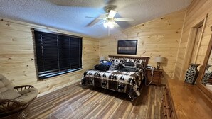 A wooden cabin bedroom with a bed, a chair, a nightstand, a lamp, and a ceiling fan. - The Smoky Mountains are OPEN FOR BUSINESS. Recently remodeled on inside.  (Sevierville)