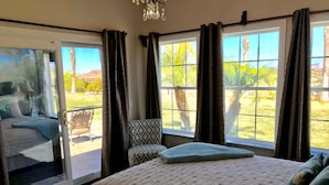 A bedroom with a large bed, a chair, and a view of the outdoors through a sliding door.