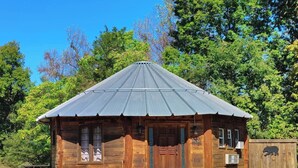 A rustic wooden cabin with a metal roof, a front door, and a small porch area with potted plants. - The Mountaineer Rustic Yurt (Genoa)