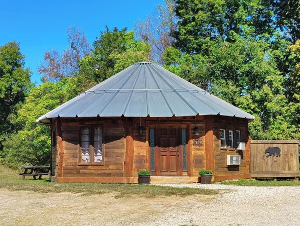 Una cabaña rústica de madera con techo metálico, puerta principal y un pequeño porche con macetas.