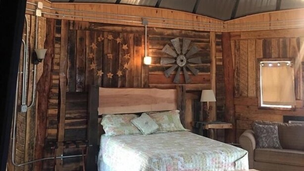 A rustic bedroom with a wooden bed, a wooden bench, a wooden ladder, and a decorative wall piece. - The Mountaineer Rustic Yurt (Genoa)