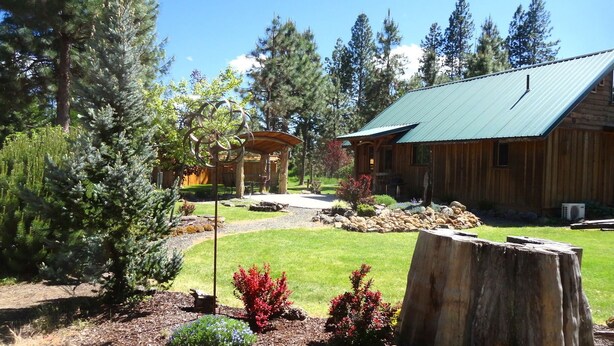 A rustic cabin with a green roof, surrounded by a well-maintained garden with various plants and a stone pathway leading to the entrance. - Red Blanket Cabin Near Crater Lake National Park (Prospect)