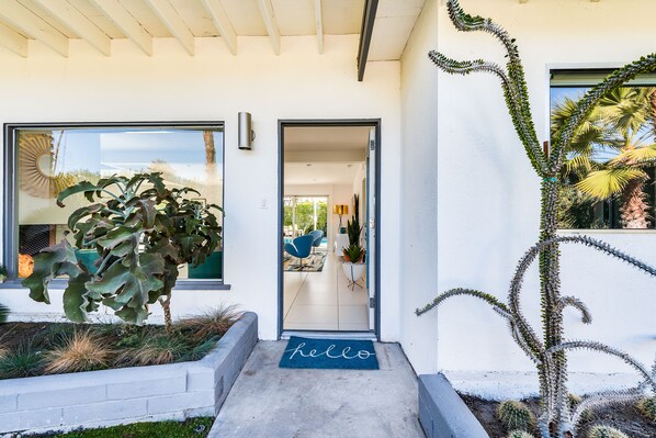 A modern house entrance with a 'hello' mat, a large window, and a well-maintained garden. - PS 6Palms: Mid-Century Gemstone Makes Palm Springs The Life! (Palm Springs)