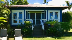 Une maison à deux étages, à l’extérieur bleu et aux ornements blancs, dotée d’un porche avec des balustrades blanches et d’un escalier menant à l’entrée.