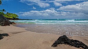 Une plage avec un ciel dégagé, des vagues et des affleurements rocheux.