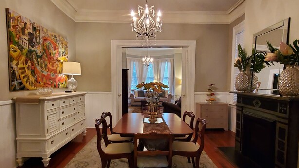 Une salle à manger agrémentée d’un lustre, d’une commode blanche et d’un tableau abstrait aux couleurs vives.