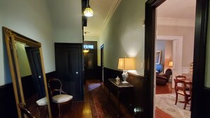 Un couloir avec un plancher en bois, un tapis, un miroir, une lampe et une chaise.