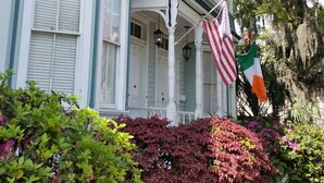 Une maison à deux étages dotée d’une baie vitrée, d’un porche avec des colonnes blanches et d’un drapeau.