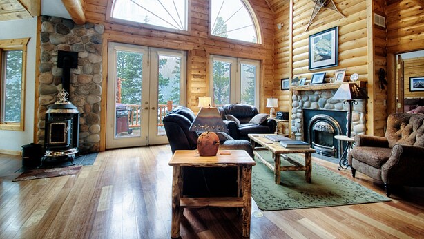 A log cabin interior with a stone fireplace, leather furniture, and large windows. - Lake Front Log Home, Amazing Mountain Views, Private Fishing and Canoeing (Idaho Springs)