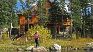 A cabin with a stone foundation and wooden upper structure, surrounded by a forest and a lake. - Lake Front Log Home, Amazing Mountain Views, Private Fishing and Canoeing (Idaho Springs)