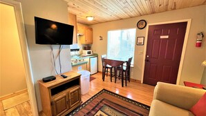 Un espacio habitable compacto con kitchenette, comedor y televisor montado en la pared.