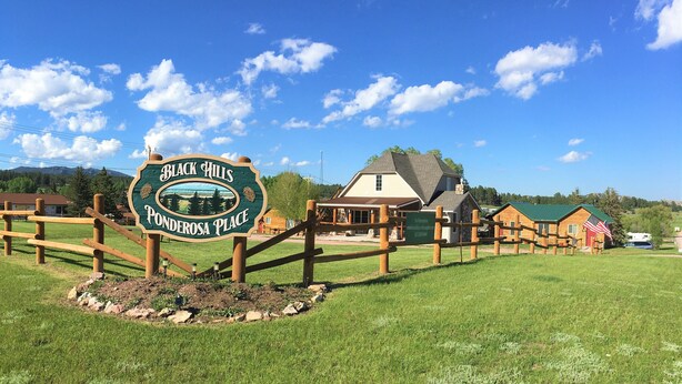 Señal de Black Hills Ponderosa Place, con una valla de madera y un edificio al fondo.