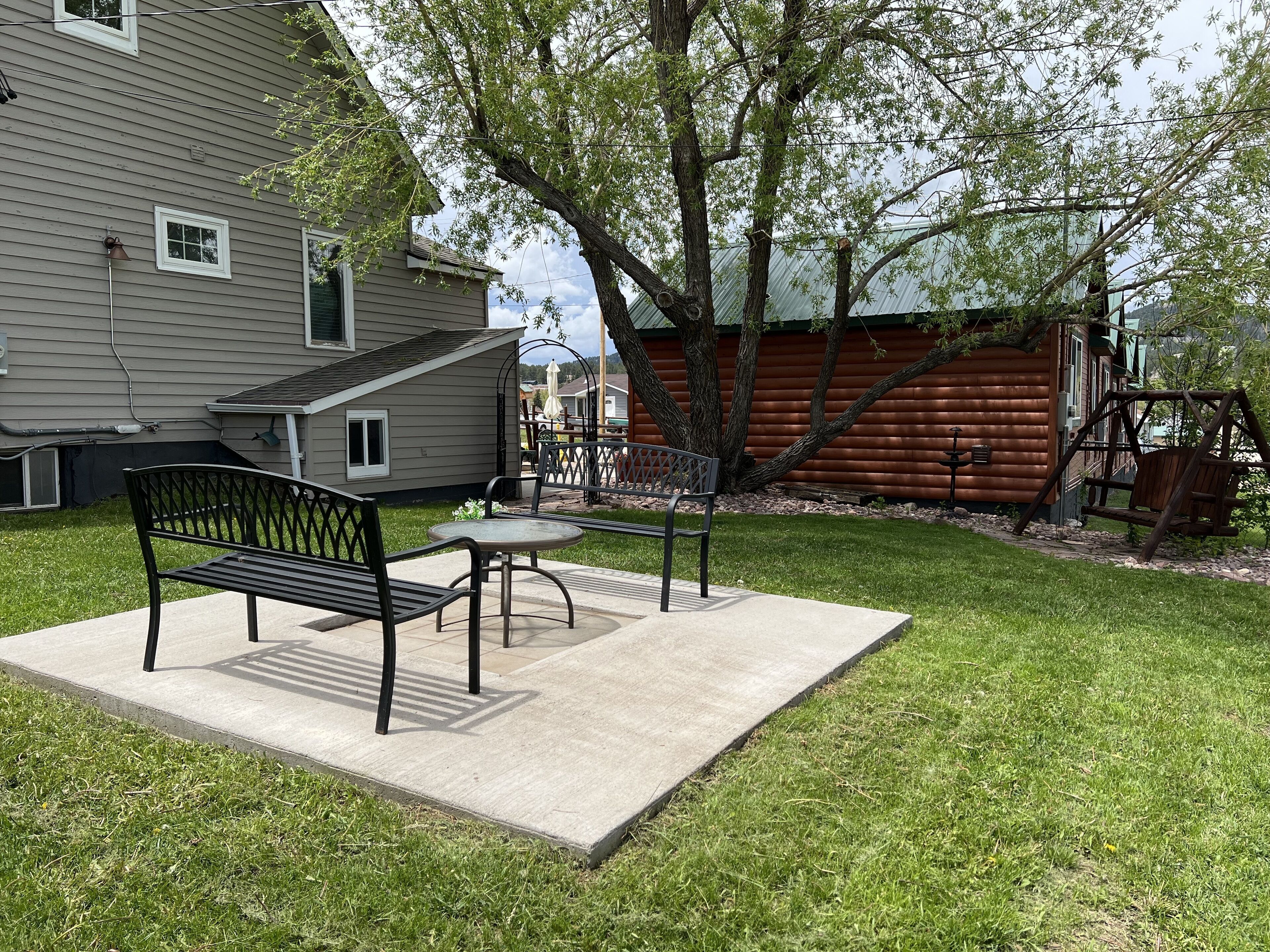 A patio area with a bench and table, surrounded by a grassy lawn and a wooden cabin.