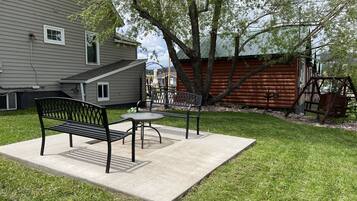 A patio area with a bench and table, surrounded by a grassy lawn and a wooden cabin.