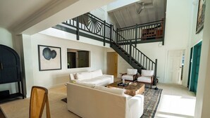 A spacious living room with a white sofa, a coffee table, and a staircase leading to an upper level. - Luxury 4 Bedroom Tobago Villa, Ocean View, Large Pool, Cabana (Mt. Irvine)