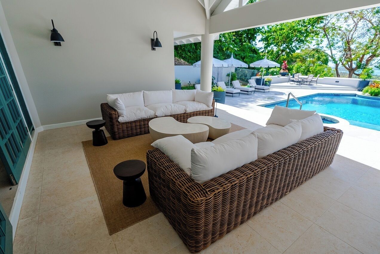 Uma área de estar moderna ao ar livre, com móveis de vime, piscina e vista para o jardim.