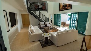 A spacious living room with a staircase, white sofas, a coffee table, and a painting on the wall. - Luxury 4 Bedroom Tobago Villa, Ocean View, Large Pool, Cabana (Mt. Irvine)