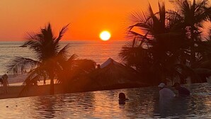 Atardecer sobre una masa de agua con palmeras y una estructura de techo de paja.