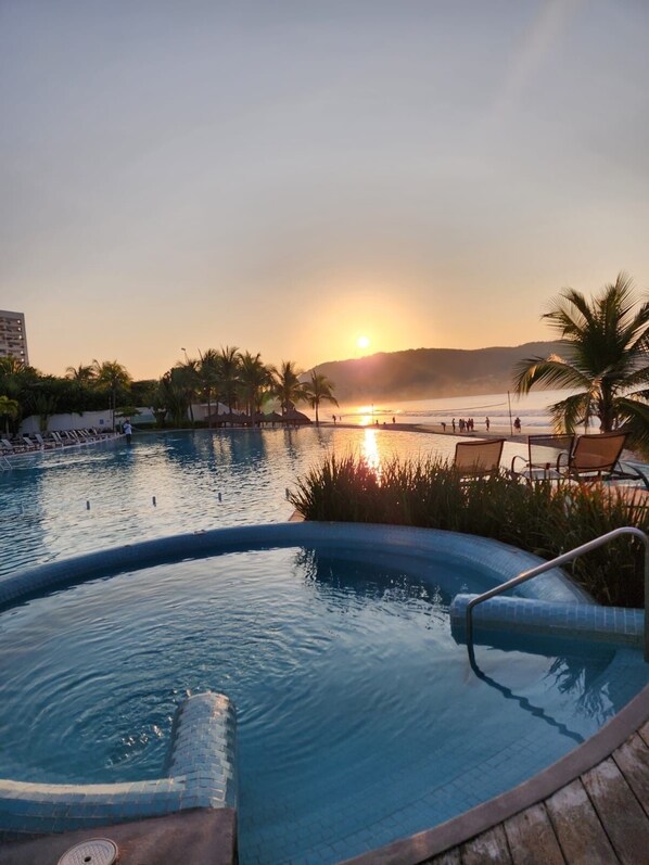 A swimming pool with a sunset view, lounge chairs, and palm trees.
