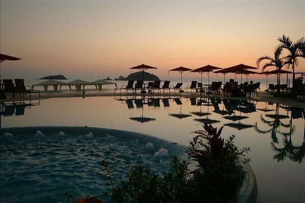 Relax by the serene pool surrounded by lounge chairs and umbrellas, with a tranquil view of the ocean in the distance.