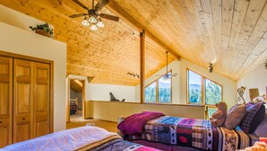 Ein gemütliches Schlafzimmer mit zwei Betten, Holzbalkendecke, Deckenventilator und großen Fenstern mit Blick ins Freie.