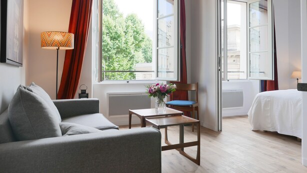 A modern hotel room with a sofa, a small table with a vase of flowers, a chair, and a bed. - LATIN QUARTER, WOODEN BEAMS, 30–60 days ahead? Ask for a private offer. C2-VAs (Paris)