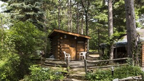 A rustic log cabin with a wooden porch and two white chairs. - Adventure U.P- Lake House on Lake Michigan (Rapid River)