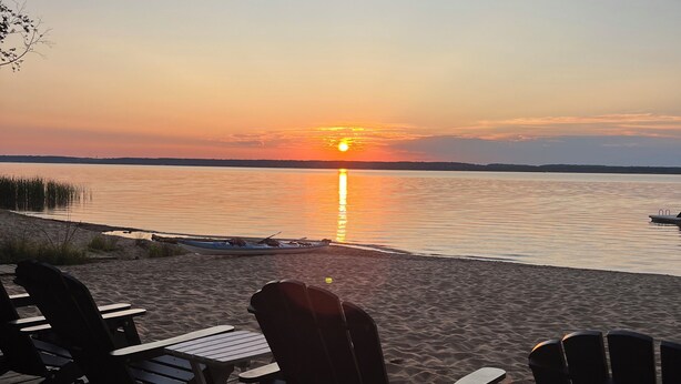 A beach with wooden chairs and a view of the sunset over water. - Adventure U.P- Lake House on Lake Michigan (Rapid River)