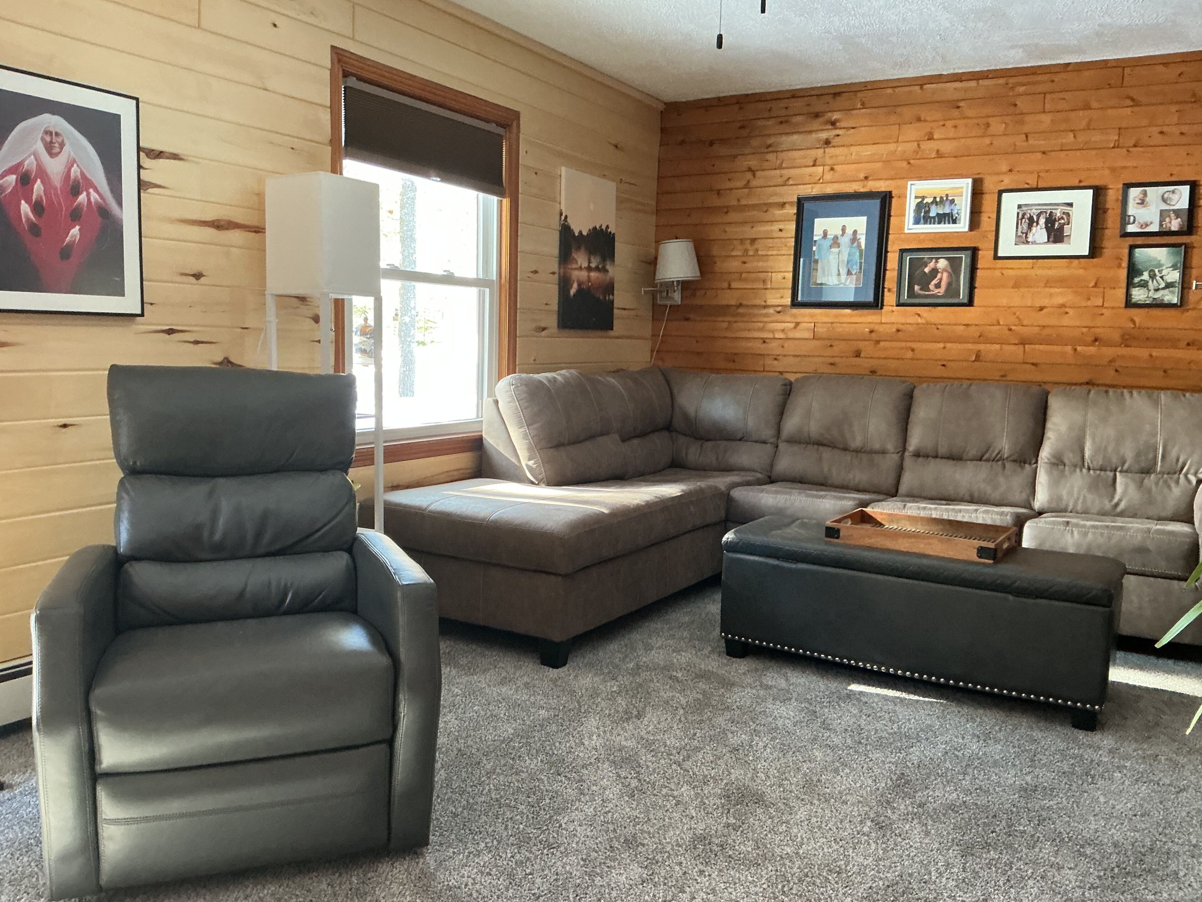 Una sala de estar con un sillón de cuero, un sofá modular y un pequeño otoman.