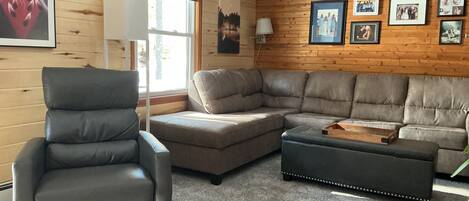 Una sala de estar con un sillón de cuero, un sofá modular y un pequeño otoman.