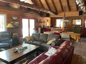 Acogedor interior de cabaña con techo de madera, comedor y sala de estar amueblada con un sofá de cuero, una mesa de centro y un sofá rojo.