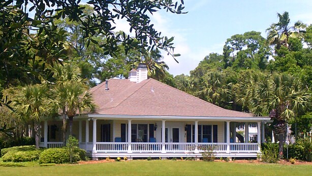 A two-story house with a porch, surrounded by a lake and palm trees.