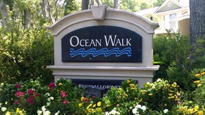 A sign for Ocean Walk with a wavy water design, surrounded by a variety of colorful flowers.